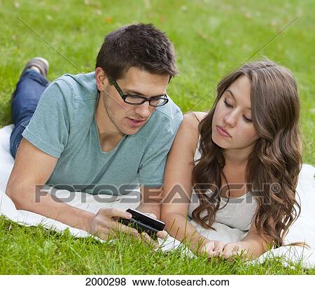 Stock Photo - Young Couple Looking At Text Messages Together In The Park; Edmonton Alberta Canada. Fotosearch
