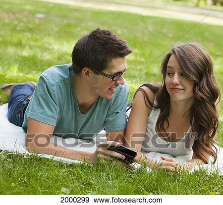 Stock Photo - Young Couple Looking At Text Messages Together In The Park; Edmonton Alberta Canada. Fotosearch