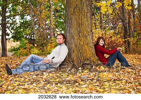 Stock Photo - Young Married Couple Leaning Against A Large Tree In A Park In Autumn; Edmonton Alberta Canada. Fotosearch