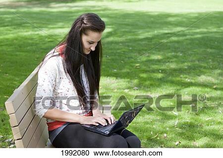 Young Woman Sitting On A Park Bench While Working On A Laptop; Edmonton Alberta Canada View Large Photo Image Stock Image - Young Woman Sitting On A Park Bench While Working On A Laptop; Edmonton Alberta Canada. Fotosearch