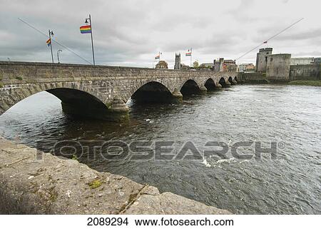 Picture - A bridge with flying flags over a river with a castle on the other side; ireland. Fotosearch
