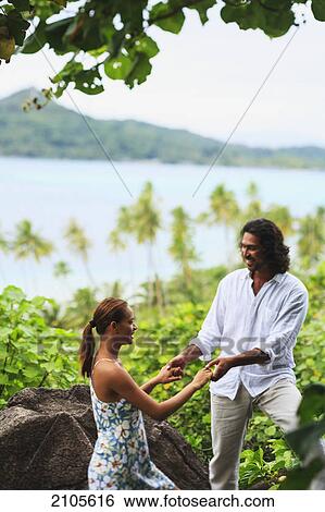 Stock Photograph - A man and woman hold hands with a view of the ocean at bora bora nui resort and spa; bora bora island society islands french polynesia south pacific. Fotosearch