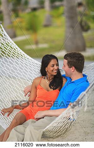 Stock Image - A man and woman sit together in a hammock at bora bora nui resort & spa; bora bora island society islands french polynesia south pacific. Fotosearch