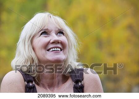 Stock Photography - A mature woman smiling in a park with autumn colours; edmonton, alberta, canada. Fotosearch