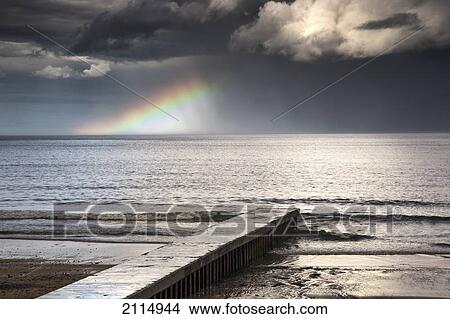 Picture - A rainbow shining in the storm clouds; blyth northumberland england. Fotosearch