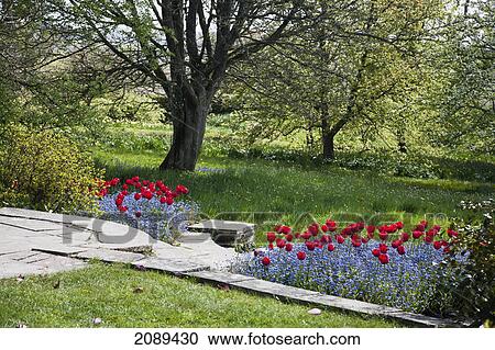 Stock Image - A stone path with a meadow and blossoming flowers at springtime; northiam, sussex, england. Fotosearch