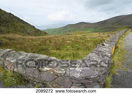 Stock Image - A stone wall between a grass field and road; ireland. Fotosearch