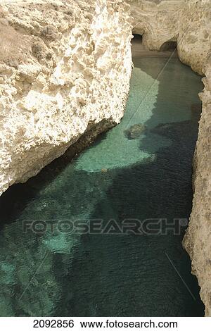 Stock Photograph - A tranquil pool of water under rock ledges; papfragas, island of milos, greece. Fotosearch