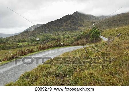 Stock Photo - A winding road over a hilly landscape and a cloudy sky; ireland. Fotosearch