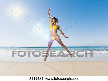 Stock Photography - A woman in a yellow bikini jumps in the air on the beach; tarifa cadiz andalusia spain. Fotosearch