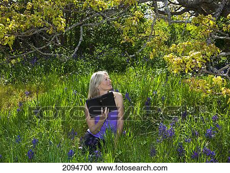 Stock Image - A woman reading her bible in a field of wildflowers; victoria, british columbia, canada. Fotosearch
