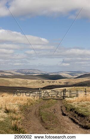 Stock Image - A wooden gate across a dirt trail with a rolling hill landscape in the distance; cheviot hills, northumberland, england. Fotosearch