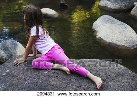 Stock Image - A young girl sitting on a rock and looking out onto the water; gold coast queensland australia. Fotosearch
