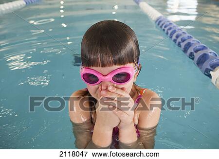 Stock Photo - A young girl wearing pink goggles and plugging her nose in a swimming pool; gold coast queensland australia. Fotosearch