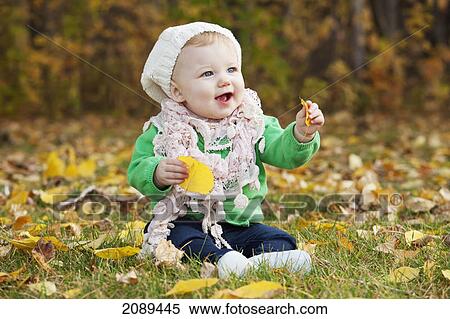 Stock Photography - An infant sitting on leaves on the ground in a park in autumn; edmonton, alberta, canada. Fotosearch