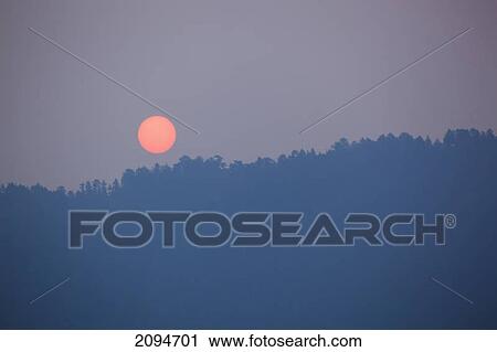 Stock Image - An orange sun rises into a smokey summer sky; desolation sound, british columbia, canada. Fotosearch
