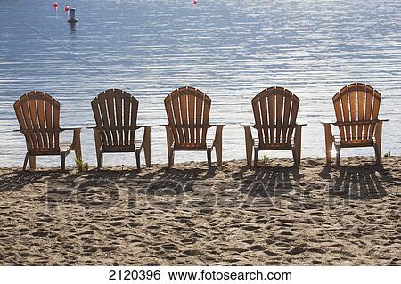 Beach chairs lined up on the shoreline of a sun reflective lake with shadows of the chairs on the sand; summerland british columbia canada View Large Photo Image Stock Photograph - Beach chairs lined up on the shoreline of a sun reflective lake with shadows of the chairs on the sand; summerland british columbia canada. Fotosearch