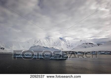 Stock Photo - Iceberg in the ocean and snow covered mountains along the coastline; antarctica. Fotosearch