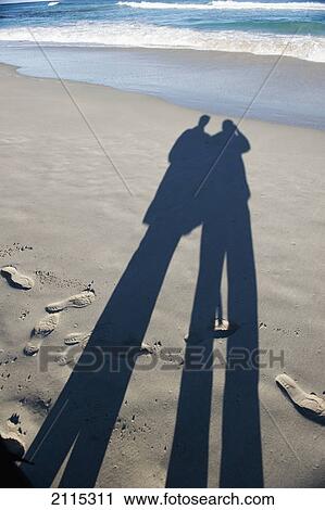 Long shadows of two people standing on a beach at the water's edge; australia View Large Photo Image Stock Image - Long shadows of two people standing on a beach at the water's edge; australia. Fotosearch