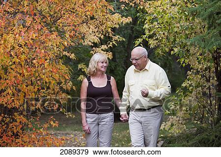 Stock Photo - Mature married couple walking together in park during fall season; edmonton, alberta, canada. Fotosearch