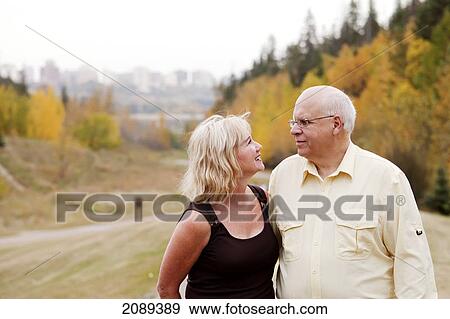 Stock Photo - Mature married couple walking together in park during fall season; edmonton, alberta, canada. Fotosearch