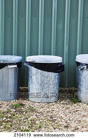Stock Photo - Metal garbage bins in a row against a metal wall; murwillumba new south wales australia. Fotosearch