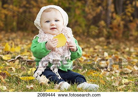 Picture - Portrait of an infant sitting on leaves on the ground in a park in autumn; edmonton, alberta, canada. Fotosearch