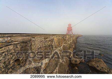 Stock Photography - Red lighthouse in the fog on the coast; south shields, tyne and wear, england. Fotosearch