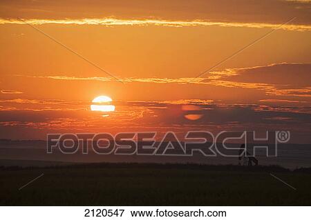 Stock Photo - Silhouette of pumpjack in a field at sunrise with orange cast sky and clouds east of airdrie; alberta canada. Fotosearch
