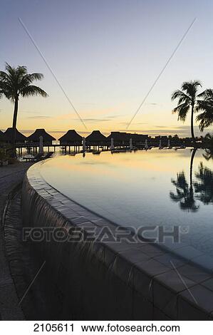 Stock Image - Sunset and palm trees reflecting in a pool at the bora bora nui resort and spa; bora bora island society islands french polynesia south pacific. Fotosearch