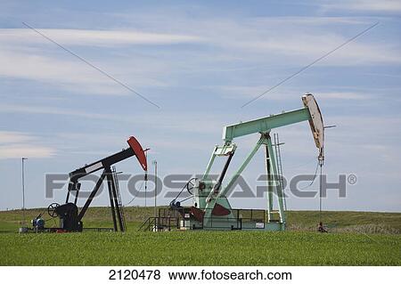 Stock Photo - Two pump jacks in a field with clouds and blue sky east of airdrie; alberta canada. Fotosearch