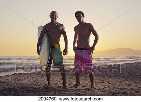 Stock Image - Two young men standing on the beach with a surfboard; tarifa, cadiz, andalusia, spain. Fotosearch