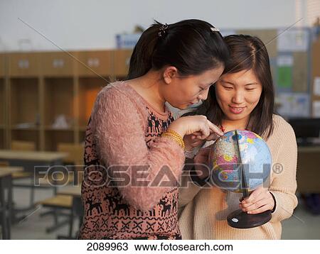Stock Image - Two young women studying a globe; beijing, china. Fotosearch