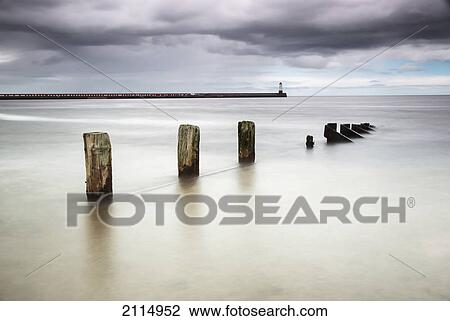 Wooden posts in the ocean with a lighthouse at the end of a pier; View Large Photo Image Stock Image - Wooden posts in the ocean with a lighthouse at the end of a pier;. Fotosearch