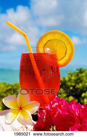 Stock Image - A Bright Red Tropical Cocktail Garnished With Flowers In Outdoor Setting.. Fotosearch