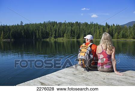 Stock Photo - A couple sits on a wooden dock at lost lake; whistler british columbia canada. Fotosearch