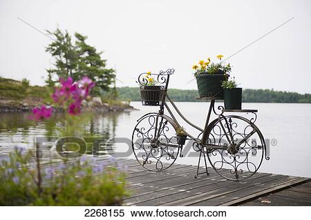 Stock Photography - A deck on a lake with a decorative flower pot in the shape of a bicycle; kenora ontario canada. Fotosearch