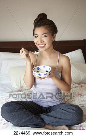 A girl sitting on her bed eating a snack from a bowl; berkeley california united states of america View Large Photo Image Stock Photo - A girl sitting on her bed eating a snack from a bowl; berkeley california united states of america. Fotosearch