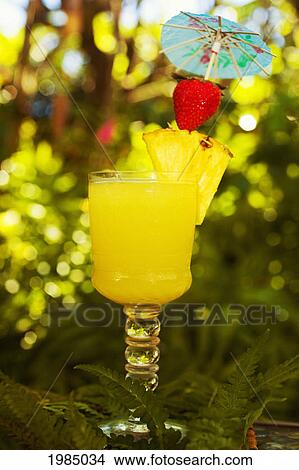 Picture - A Tropical Cocktail Garnished With Fruit In An Outdoor Setting.. Fotosearch