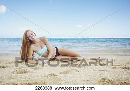 Stock Photo - A young woman laying on the sand at the ocean's edge; kauai hawaii united states of america. Fotosearch