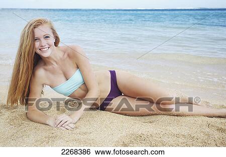 Stock Photograph - A young woman laying on the sand at the ocean's edge; kauai hawaii united states of america. Fotosearch