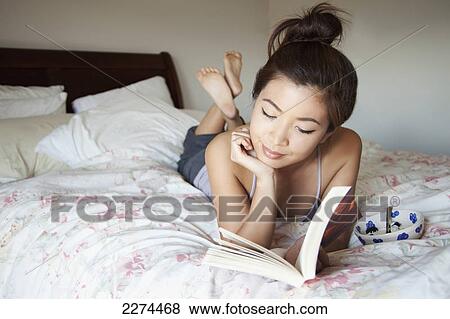 A young woman lays on her bed reading a book; berkeley california united states of america View Large Photo Image Stock Photo - A young woman lays on her bed reading a book; berkeley california united states of america. Fotosearch
