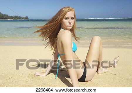 A young woman sitting in the sand along the ocean at the coast; kauai hawaii united states of america View Large Photo Image Picture - A young woman sitting in the sand along the ocean at the coast; kauai hawaii united states of america. Fotosearch