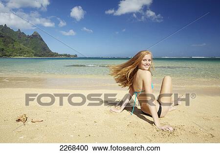 A young woman sitting in the sand along the ocean at the coast; kauai hawaii united states of america View Large Photo Image Stock Image - A young woman sitting in the sand along the ocean at the coast; kauai hawaii united states of america. Fotosearch