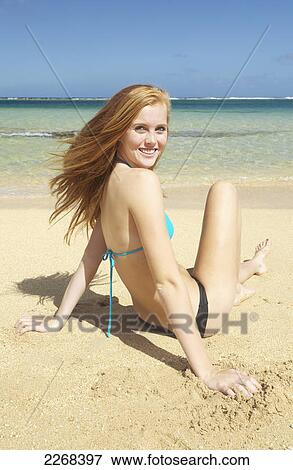 A young woman sitting in the sand along the ocean at the coast; kauai hawaii united states of america View Large Photo Image Stock Photo - A young woman sitting in the sand along the ocean at the coast; kauai hawaii united states of america. Fotosearch