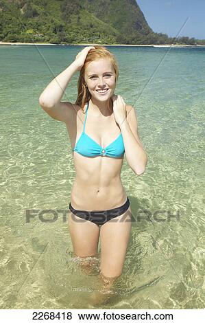 Stock Photo - A young woman standing in the shallow water of the ocean along the coast; kauai hawaii united states of america. Fotosearch