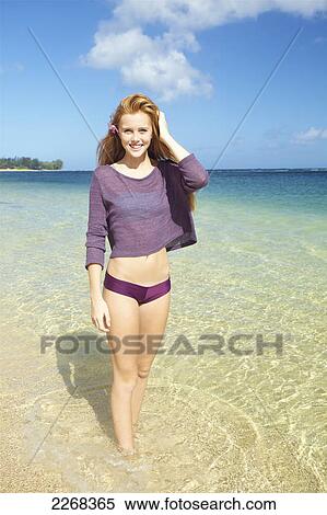 Stock Photography - A young woman standing in the shallow water along a beach; kauai hawaii united states of america. Fotosearch