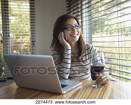A young woman talking on the phone while holding a glass of wine and sitting in front of a computer; berkeley california united states of america View Large Photo Image Stock Image - A young woman talking on the phone while holding a glass of wine and sitting in front of a computer; berkeley california united states of america. Fotosearch