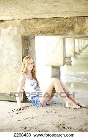 A young woman with long red hair sits in the sand under a bridge at the water's edge; kauai hawaii united states of america View Large Photo Image Stock Image - A young woman with long red hair sits in the sand under a bridge at the water's edge; kauai hawaii united states of america. Fotosearch