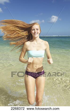 Stock Image - A young woman with long red hair running down a beach; kauai hawaii united states of america. Fotosearch